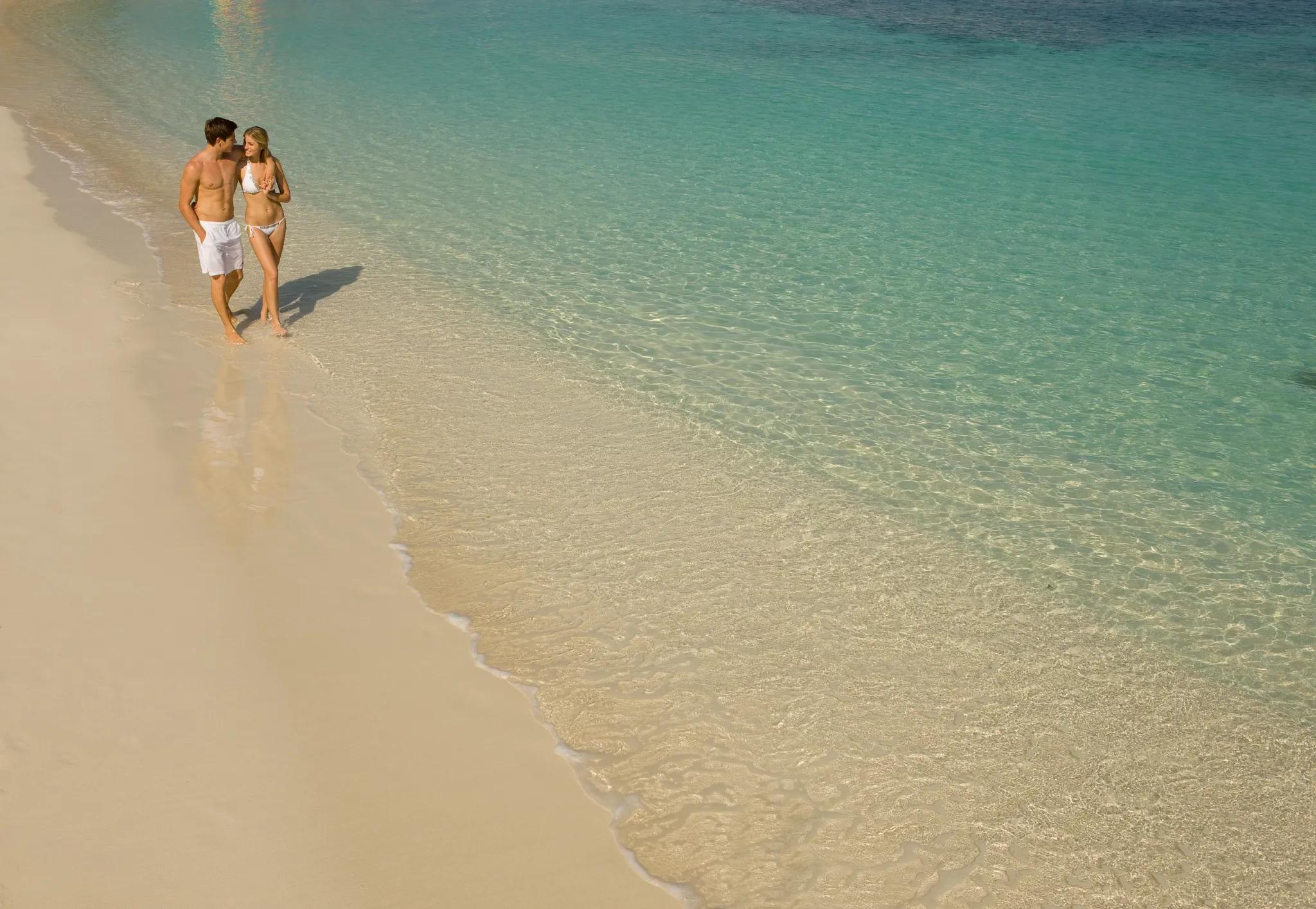 Couple walking along a white-sand beach with clear turquoise water at Secrets St. James Montego Bay, perfect for romantic getaways.