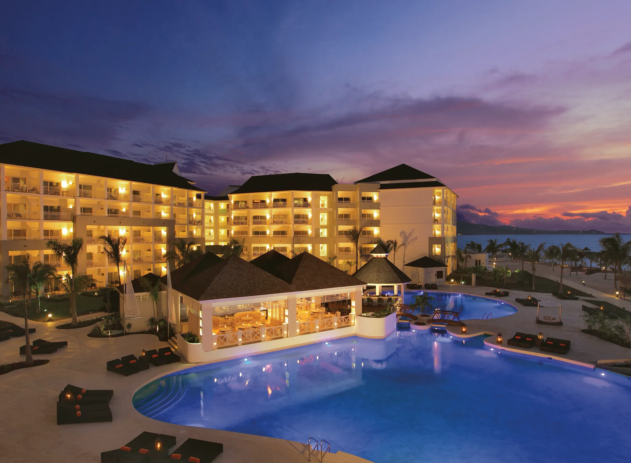 Illuminated resort pool at sunset with glowing lights at Secrets St. James Montego Bay, creating a romantic evening atmosphere.