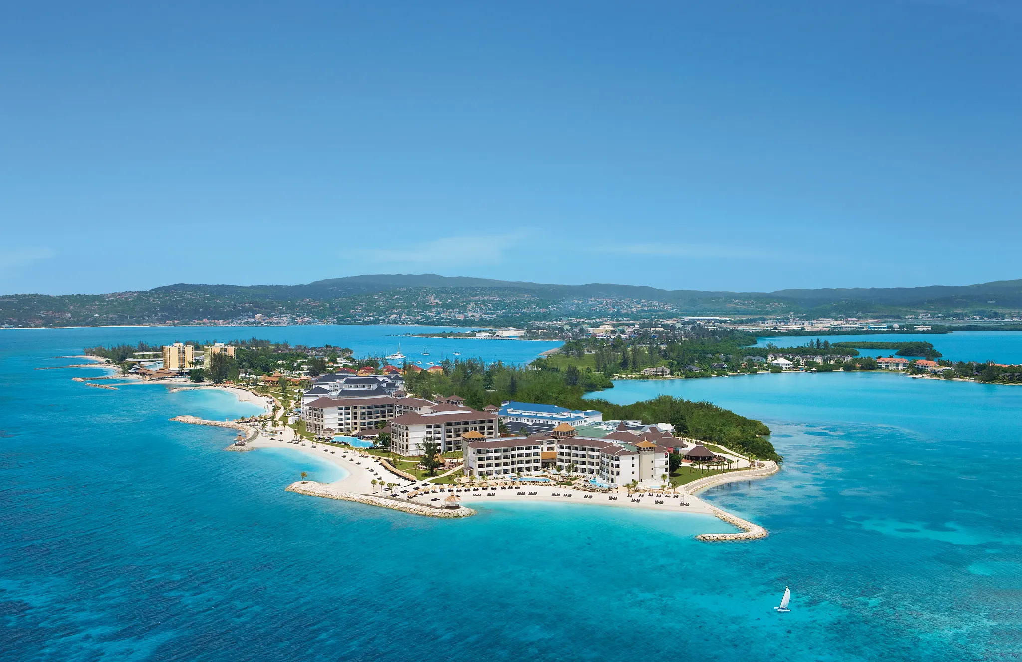 Panoramic aerial of Secrets St. James Montego Bay showcasing beachfront buildings, pools, and the vibrant blue sea.