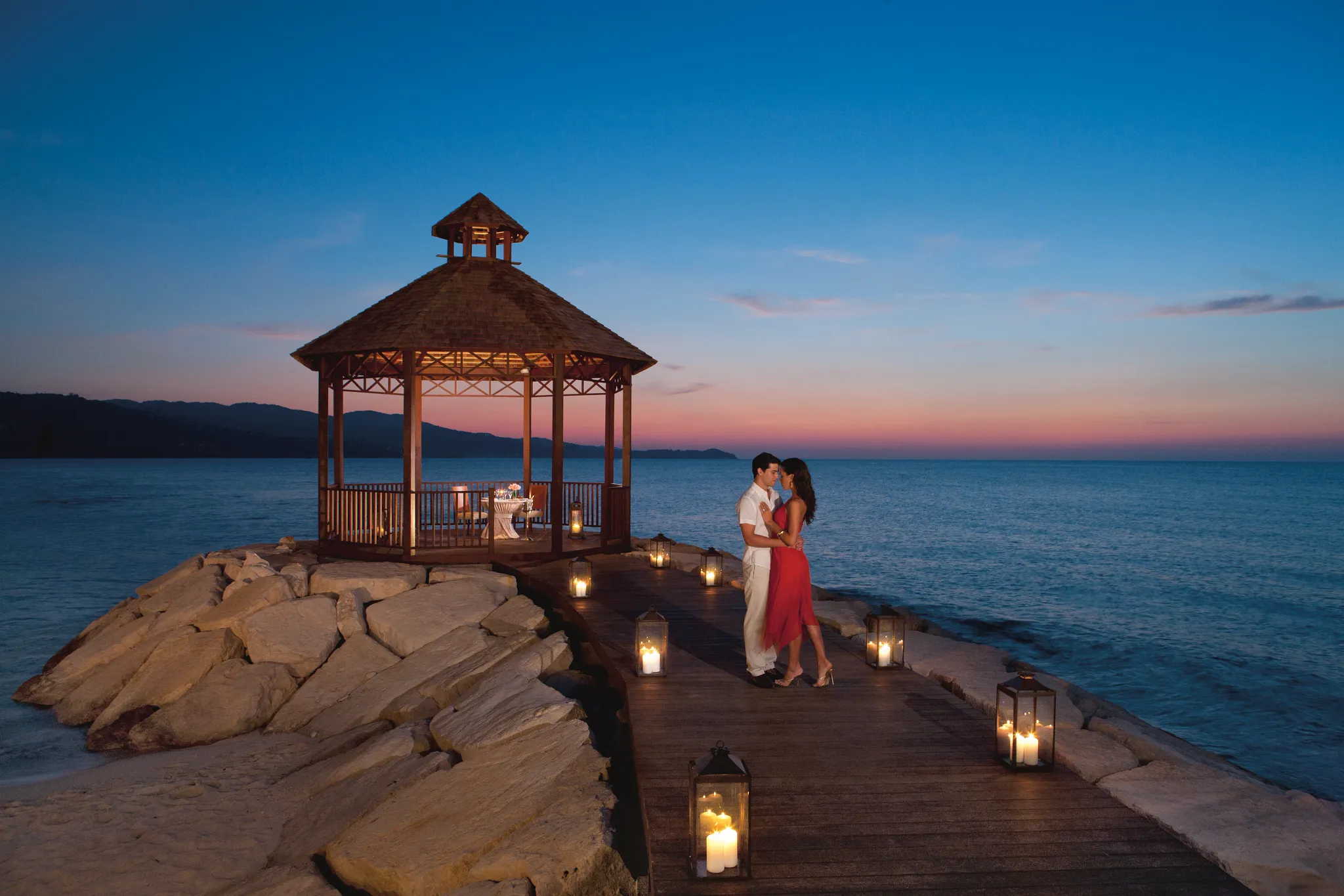 Couple enjoying a candlelit private dinner in a gazebo over the ocean at Secrets St. James Montego Bay at sunset.